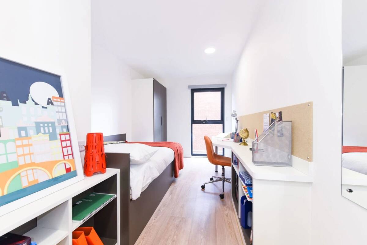 Una habitación de hotel moderna con cama, escritorio y silla, un ventanal grande y un cuadro con vistas a la ciudad.