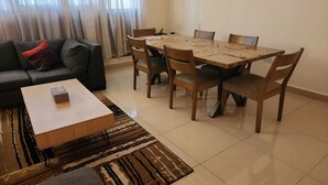 Ein Wohnzimmer mit einer Couch, einem Couchtisch, einem Esstisch mit Stühlen und einem gemusterten Teppich.