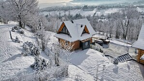 Une cabane en bois, dotée d’un toit en pente, entourée d’arbres couverts de neige et avec une chaîne de montagnes en arrière-plan.