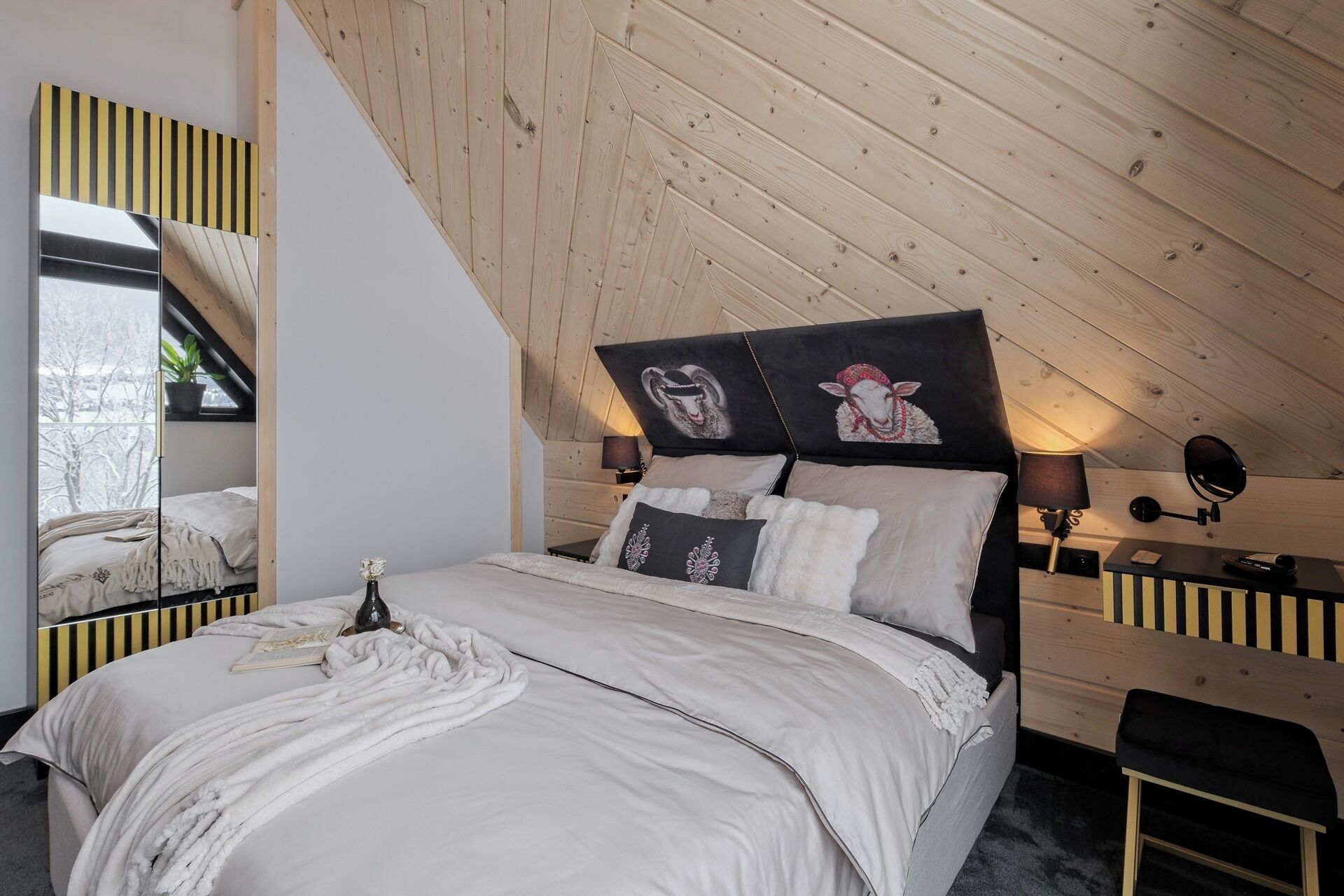 A bedroom with a sloped ceiling, a bed with white bedding, two bedside lamps, and a mirror with a striped frame.