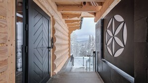 Un couloir en bois, avec des portes noires et un motif circulaire sur le mur, qui mène à un paysage enneigé.