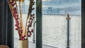 Une table ornée d’un vase contenant des plantes séchées et d’un verre à vin, donnant sur un paysage montagneux enneigé grâce à de grandes fenêtres.