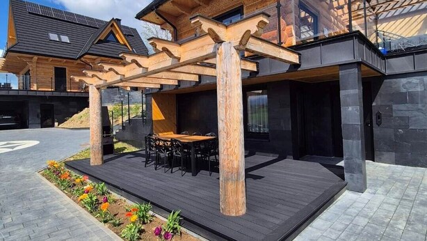 Une maison moderne dotée d’une pergola en bois, d’un espace salon extérieur et d’un jardin.