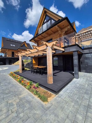 Une maison moderne dotée d’une pergola en bois, d’un espace salon extérieur et d’un jardin.
