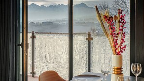 Une table à manger ornée d’un vase contenant des plantes séchées et d’un verre à vin, donnant sur un paysage enneigé avec des montagnes.