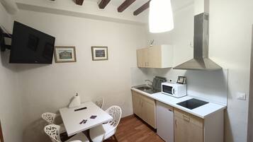 A compact kitchen with a microwave, sink, and wooden cabinets. There is a dining table with chairs and a hanging light fixture.