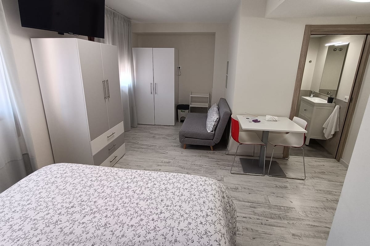 A hotel room with a bed, a desk, a chair, a wardrobe, a TV, and a bathroom.