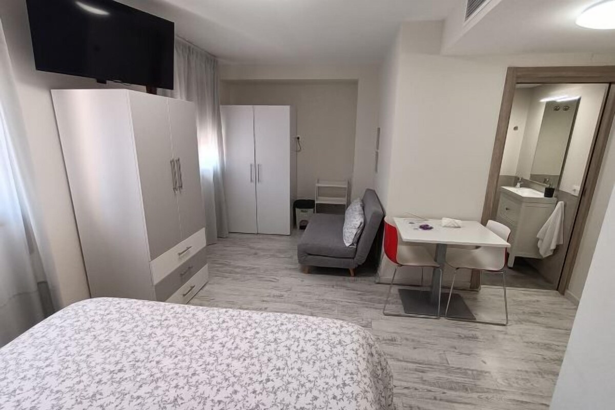 A modern hotel room with a bed, a desk, a chair, a TV, a wardrobe, and a bathroom.
