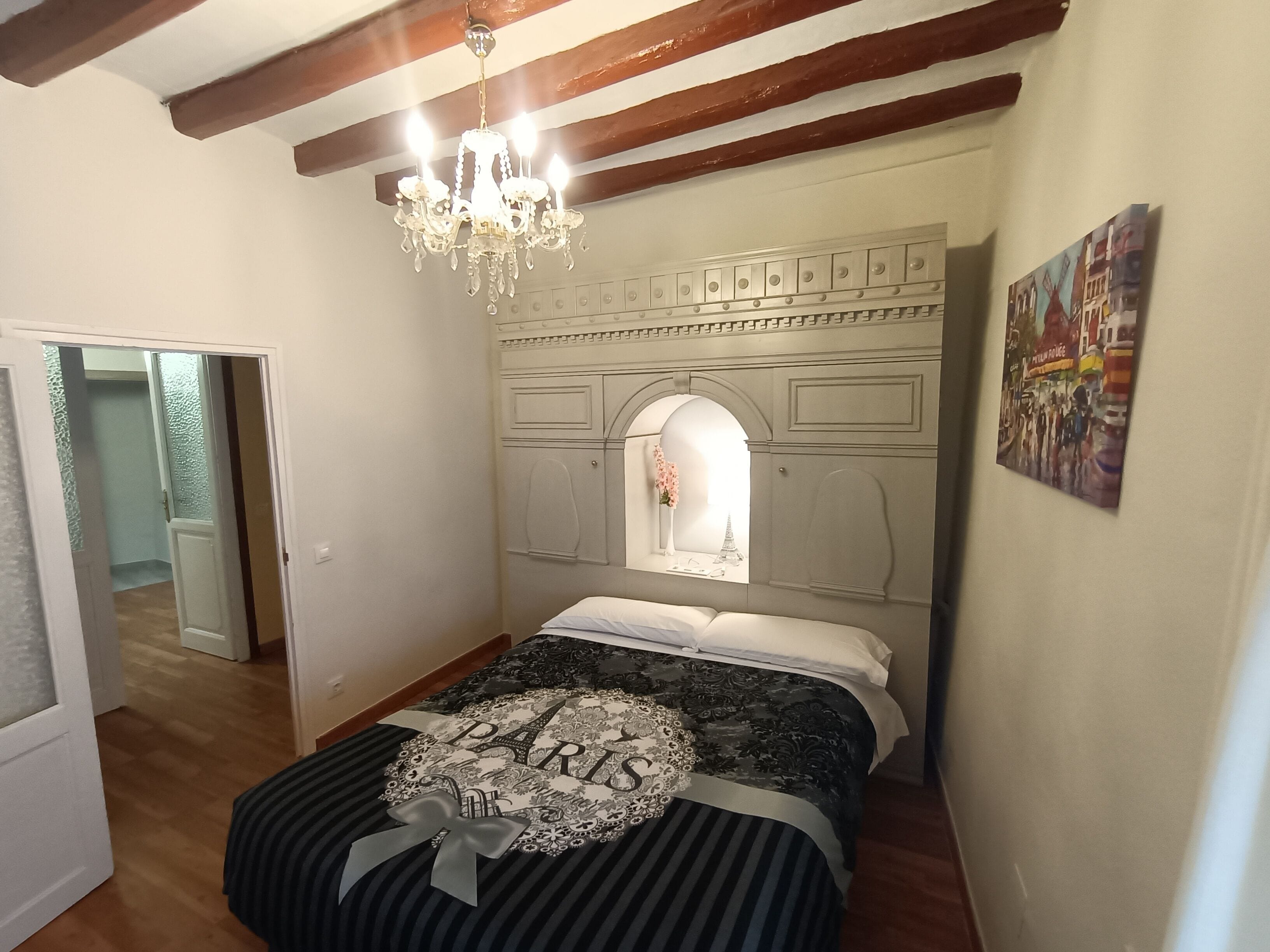A bedroom with a bed, a chandelier, a decorative headboard, and a painting on the wall.