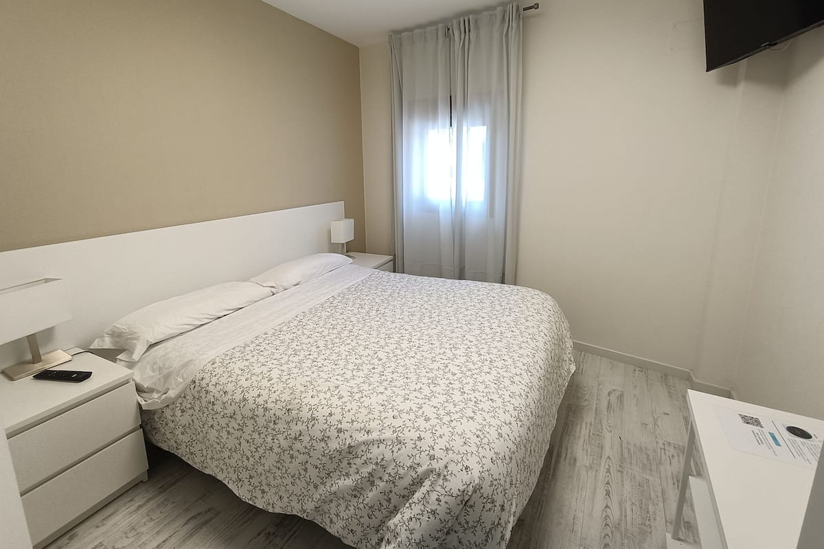 A hotel room with a bed, a nightstand, a TV, and a window with curtains.