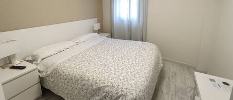 Una habitación de hotel con una cama, una mesita de noche, un televisor y una ventana con cortinas.