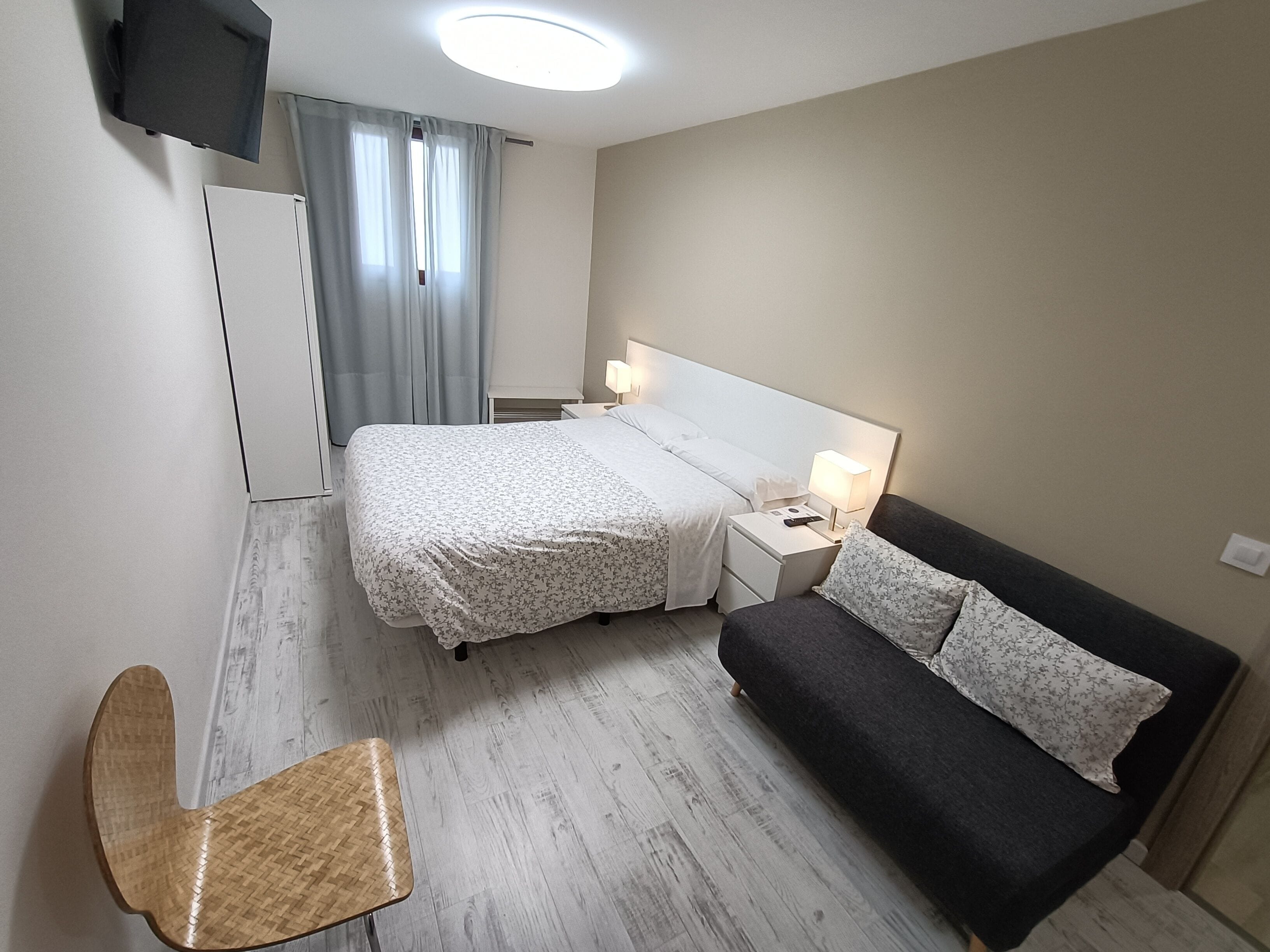 Et hotelværelse med en seng, et natbord med en lampe, en stol og et fjernsyn ophængt på væggen.