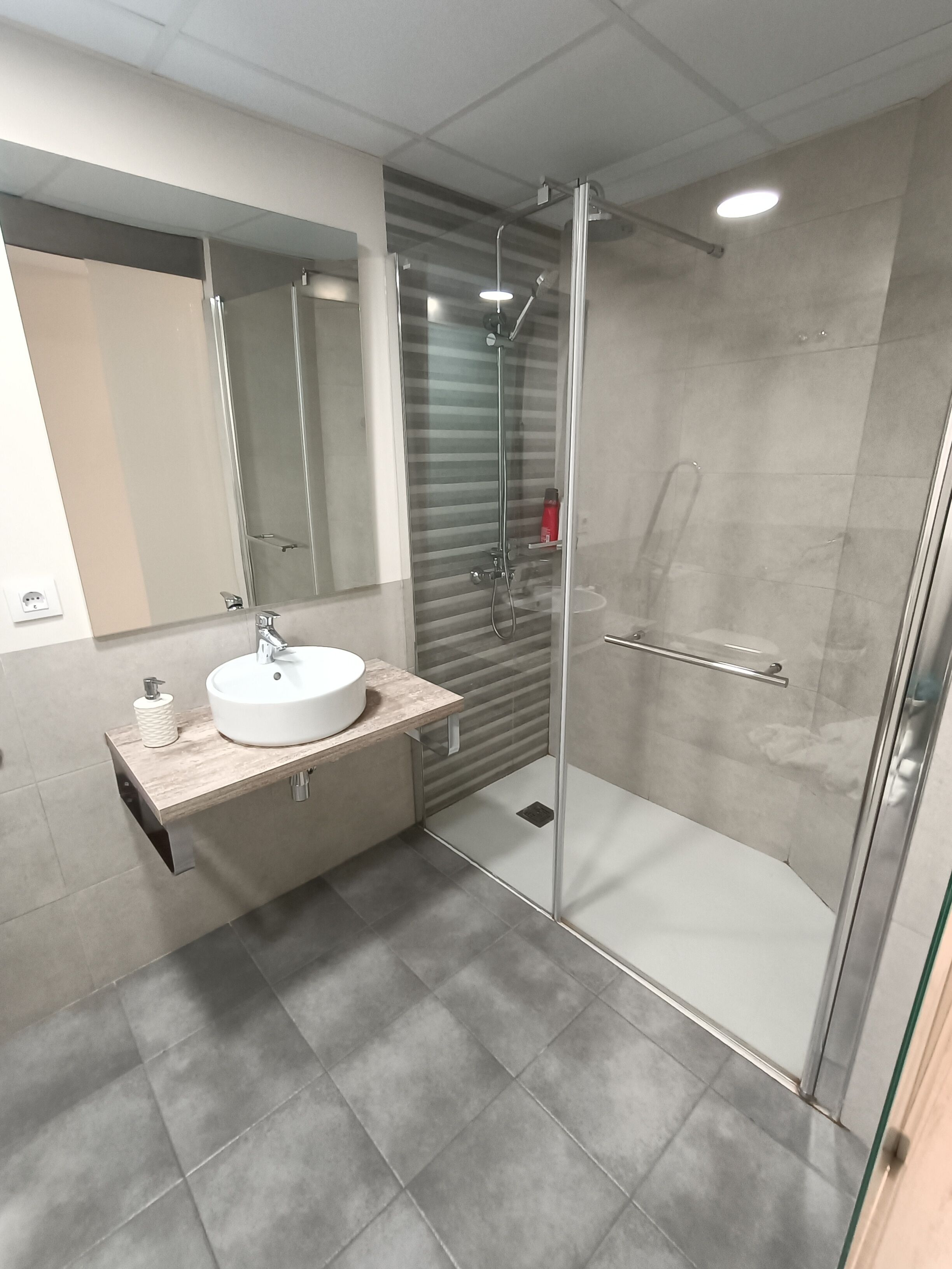 Een moderne badkamer met een douchecabine van glas, een wastafel met een marmeren blad en een spiegel boven de wastafel.