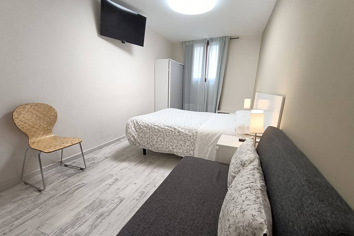 A bedroom with a bed, a chair, a desk, a lamp, and a television.