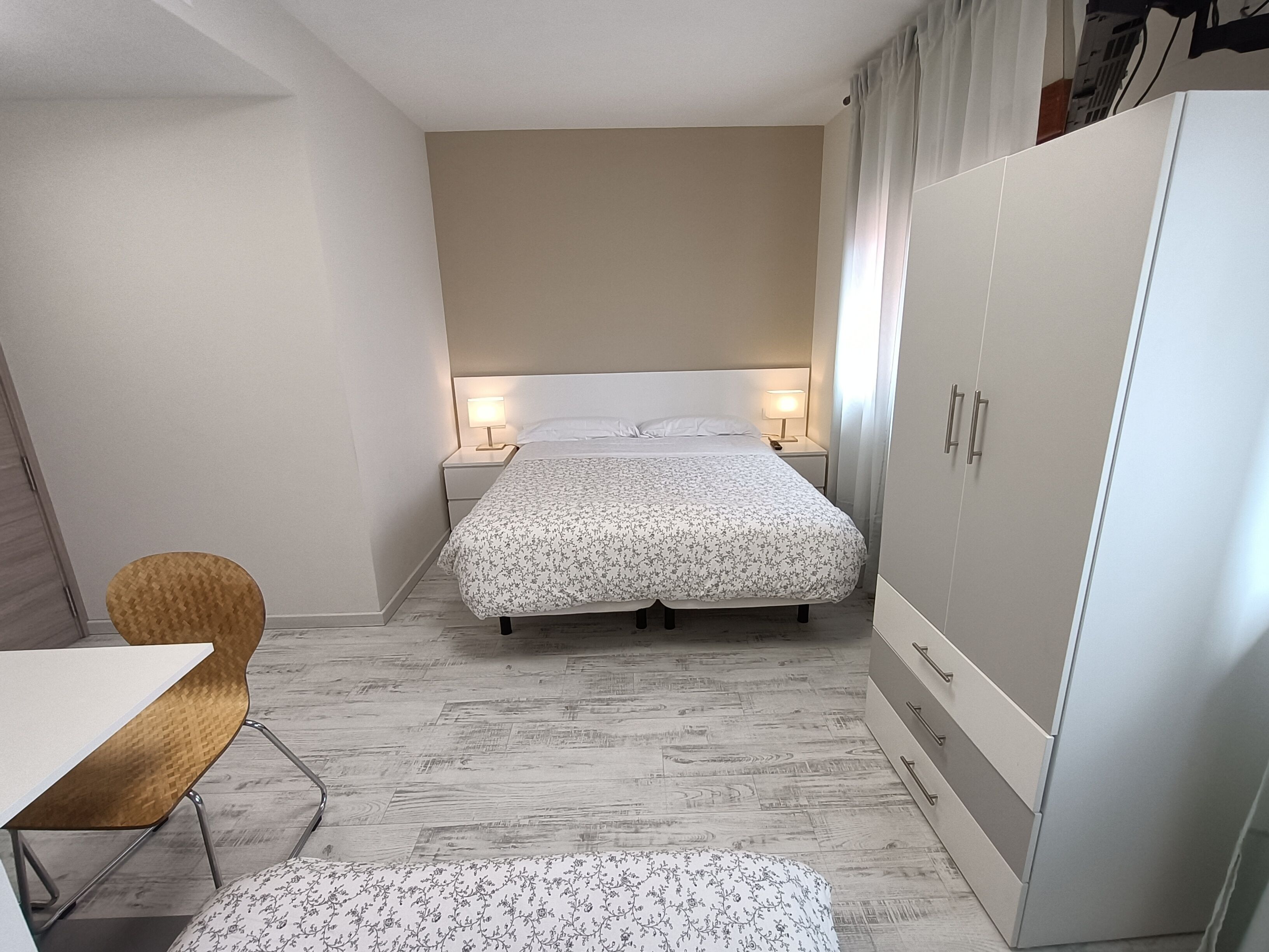 Un dormitorio pequeño y ordenado con cama, mesitas de noche, armario y una silla.