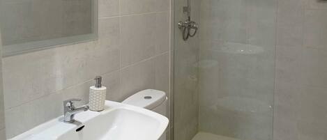 Un baño moderno con ducha de vidrio, lavamanos blanco y un inodoro.