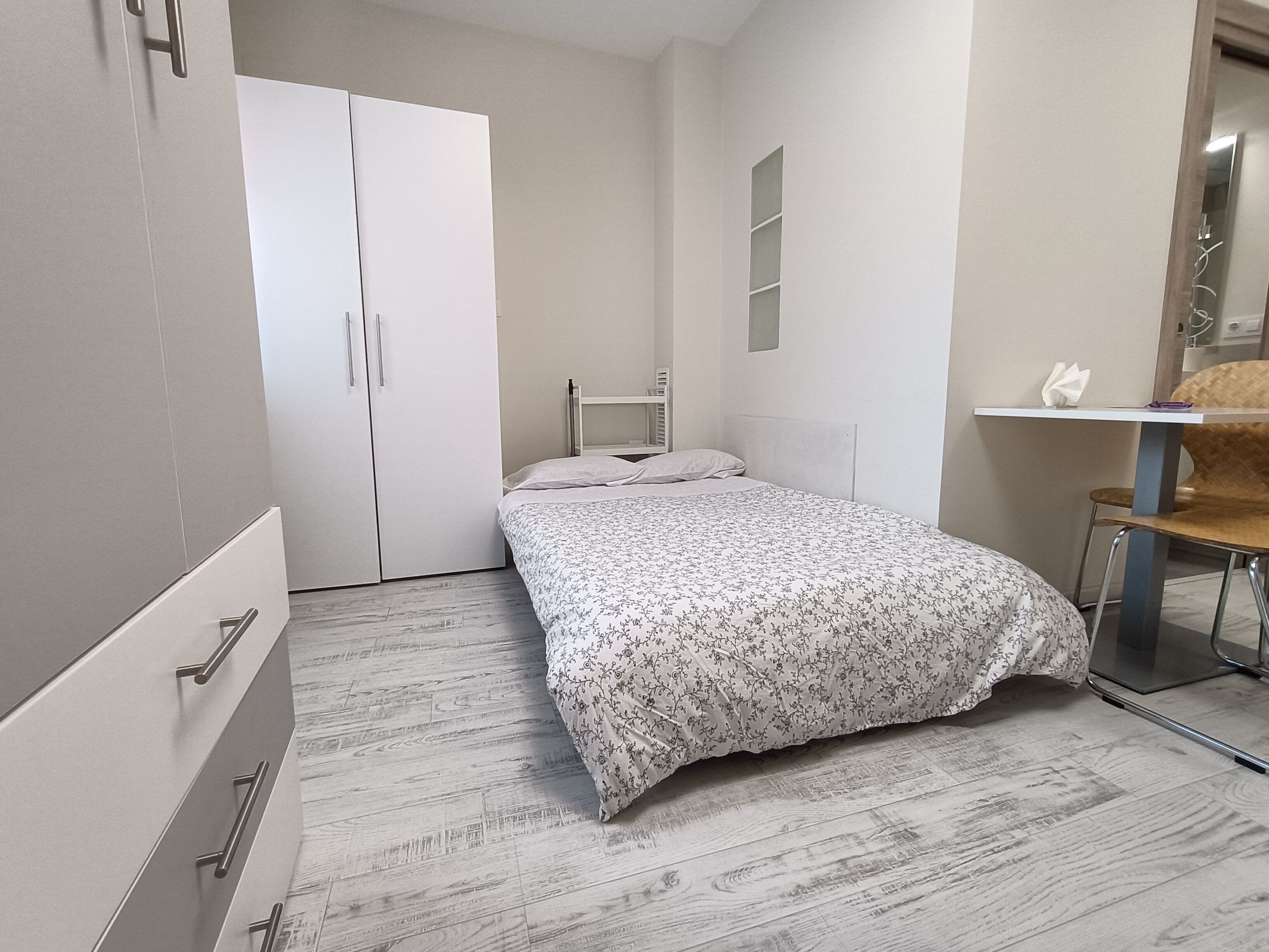 Un dormitorio con cama, armario, escritorio y silla.