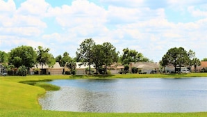 A golf course with a pond, houses in the background, and a clear sky. - Stress-Free Disney Stay-Private Pool & Fenced Yard (Kissimmee)