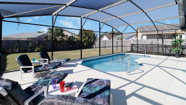 A covered outdoor swimming pool area with lounge chairs and a table. - Stress-Free Disney Stay-Private Pool & Fenced Yard (Kissimmee)