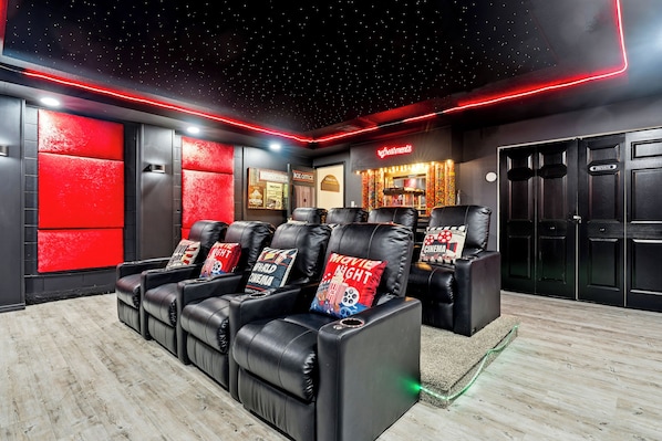 A home theater with leather reclining chairs, a starry ceiling, and a neon sign.