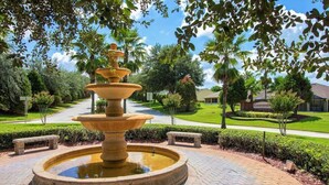 Une fontaine en pierre à plusieurs niveaux, située dans un jardin aménagé, avec des bancs et un panneau indiquant « Country Club ».