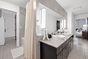 A modern bathroom with a double sink vanity, a large mirror, and a shower area.