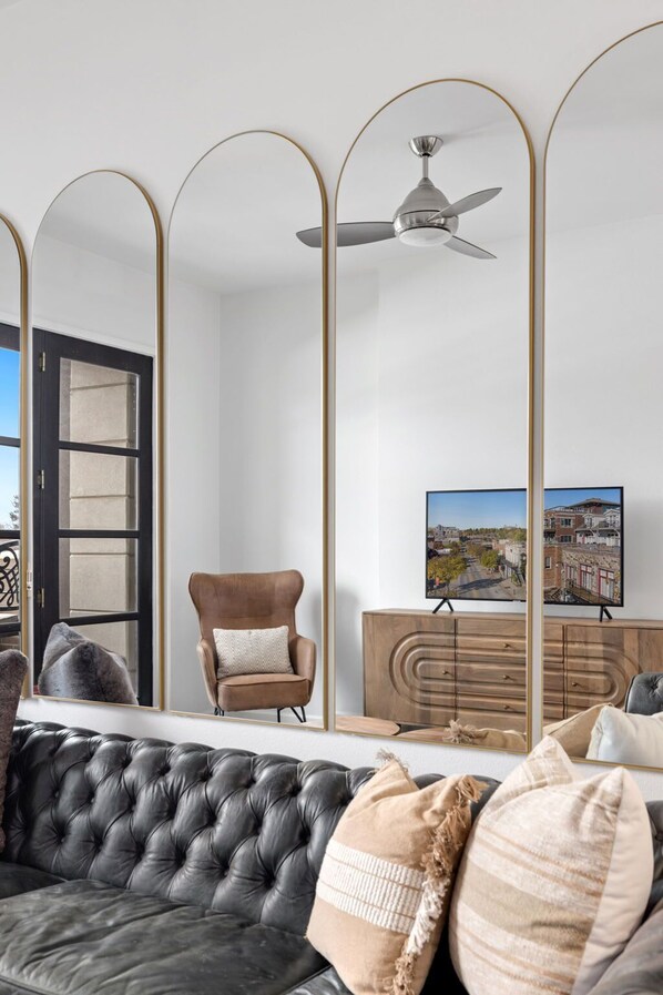 A modern living room with a black leather sofa, a brown armchair, a wooden cabinet, and a television displaying a cityscape.