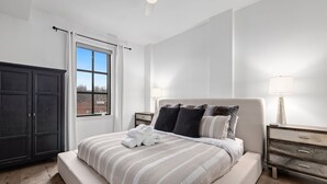 Une chambre à coucher avec un grand lit, une armoire sombre, une fenêtre avec des rideaux et une table de chevet avec une lampe.
