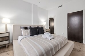 A neatly made bed with striped bedding, a bedside lamp, and a dark wooden door.