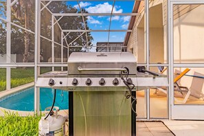 A gas grill with a stainless steel finish, a control panel with multiple knobs, and a gas tank with a label. - Perfect Family Disney Escape: Pool & Games (Kissimmee)