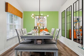 A dining area with a table set for four, chairs, a hanging light fixture, and a green accent wall. - Perfect Family Disney Escape: Pool & Games (Kissimmee)
