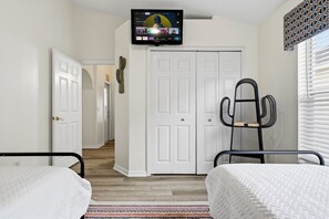 A bedroom with two beds, a television mounted on the wall, a cactus decoration, and a door leading to another room. - Perfect Family Disney Escape: Pool & Games (Kissimmee)
