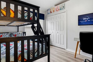 A child's bunk bed with colorful bedding, a white door, and a wall-mounted television displaying Disney+.