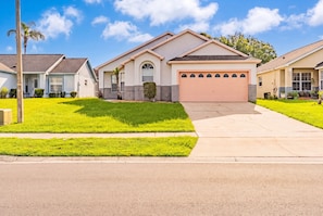 A residential house with a garage, a well-maintained lawn, and a clear sky. - Perfect Family Disney Escape: Pool & Games (Kissimmee)