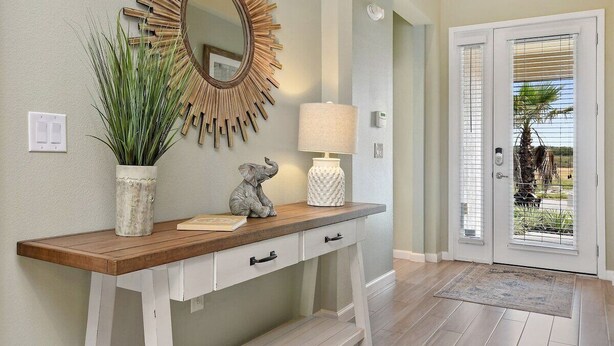 A hallway with a wooden console table, a mirror with a sunburst frame, a lamp, and a potted plant. - Magical Disney Villa • Sunny Pool, Spa & Game Room (Kissimmee)