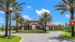 A gated entrance with a red yield sign, a one-way sign, and a building with a tiled roof and arched entrance. - Luxury Resort Villa with Pool, Spa – Perfect for Families! (Davenport)
