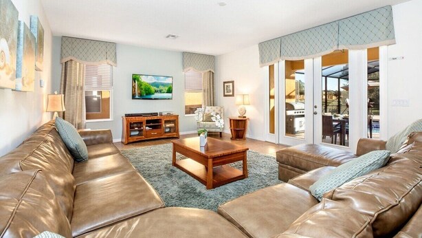 A spacious living room with a leather sofa, a wooden coffee table, and a television. - 6BR Disney Area Villa, South Facing Pool, Spa, Game Room (Davenport)