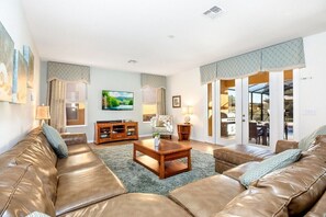 A spacious living room with a leather sofa, a wooden coffee table, and a television. - 6BR Watersong Resort Villa with South-Facing Pool & Spa Near Disney (Davenport)