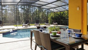 A covered outdoor area with a pool, seating, and a table set for dining. - 6BR Disney Area Villa, South Facing Pool, Spa, Game Room (Davenport)