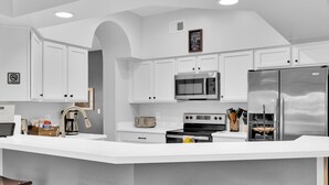 Une cuisine moderne avec des meubles blancs, un grand îlot central, des appareils en acier inoxydable et des tabourets en bois.