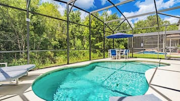 Una piscina con cerramiento de vidrio, rodeada de sillas de descanso y una zona de patio.