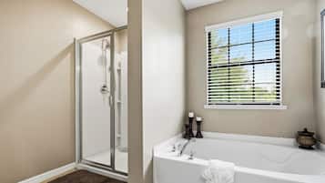 Un baño con cabina de ducha de vidrio, bañera y ventana con persianas.