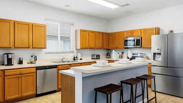 A modern kitchen with wooden cabinets, stainless steel appliances, a central island with stools, and a window with blinds.