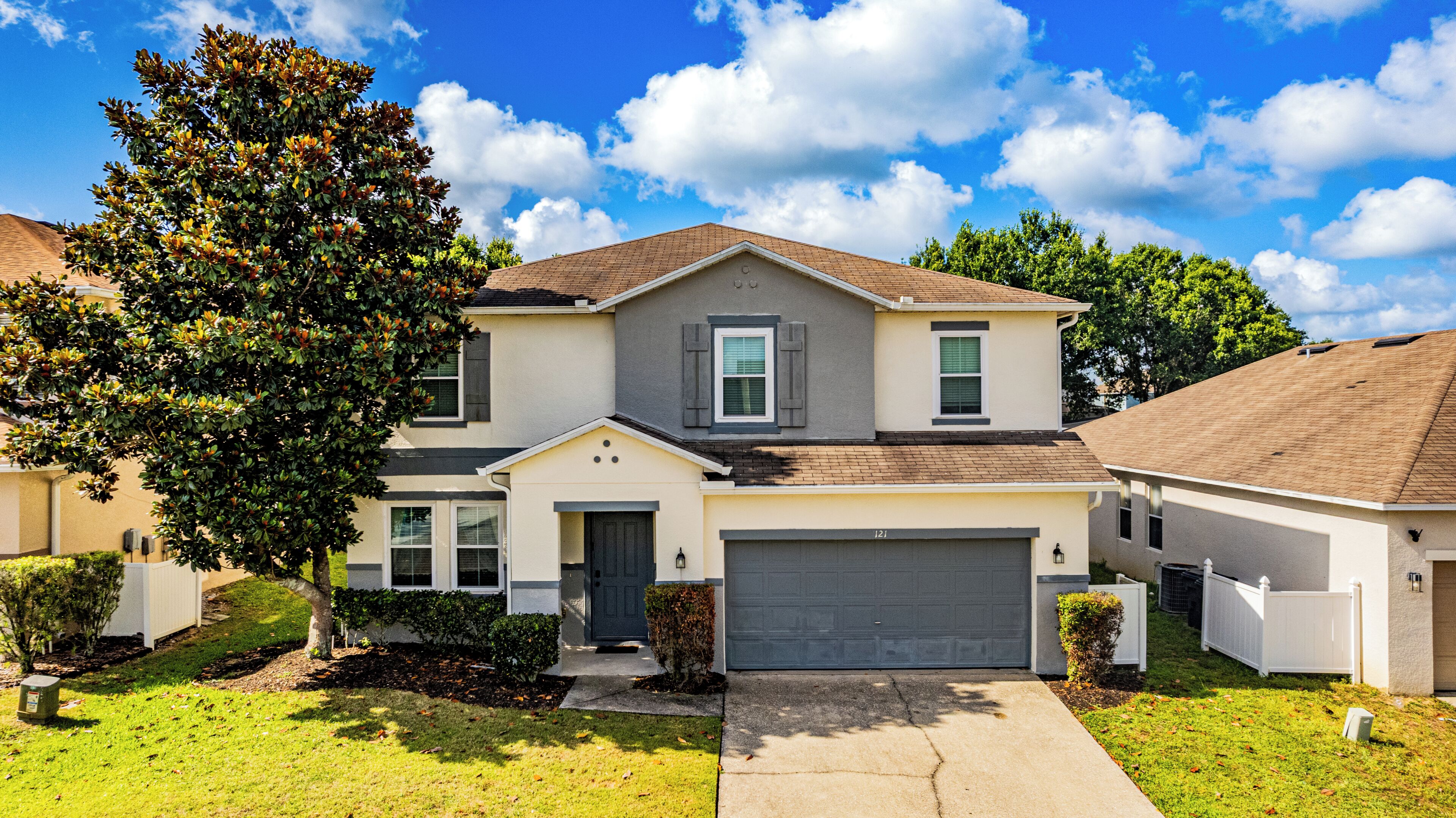 A two-story house with a garage, a front yard, and a tree.