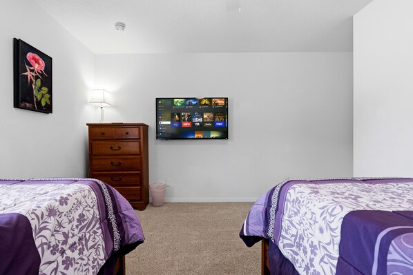 A bedroom with two beds, a dresser, a wall-mounted TV, and a framed picture.