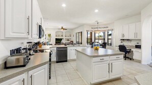 Una cocina amplia con armarios blancos, una isla central y un comedor.