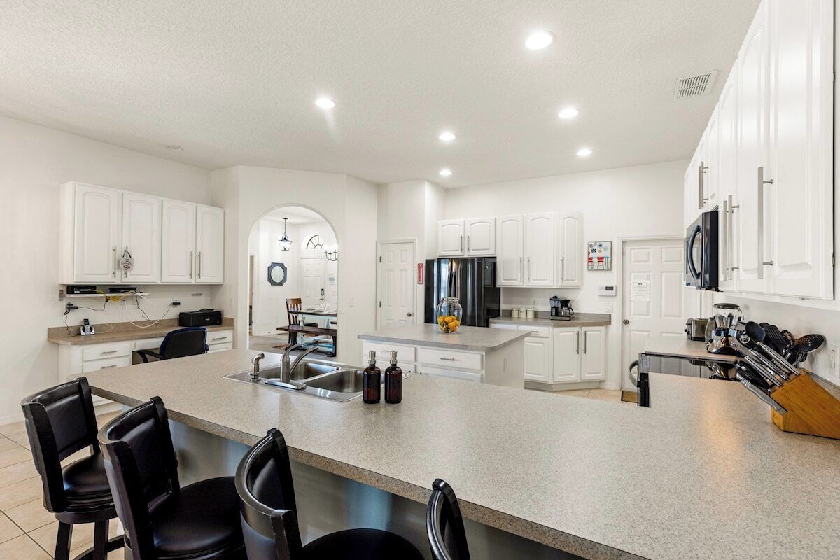 A modern kitchen with white cabinets, a central island with bar stools, stainless steel appliances, and a visible backsplash.
