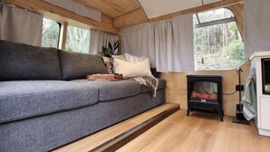 A cozy interior with a curved ceiling, a sofa, a fireplace, and large windows. - Escape to a unique retreat with Miss Beddy, recently renovated Bedford bus  (Mount Helen)
