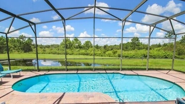 A covered swimming pool with a view of a green landscape and a small body of water. - Stunning 4BR Disney Villa w/ Pool & Arcade (Clermont)