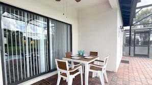A dining area with a table and chairs, a sliding glass door, and a covered outdoor space with a view of the surroundings. - Stunning 4BR Disney Villa w/ Pool & Arcade (Clermont)